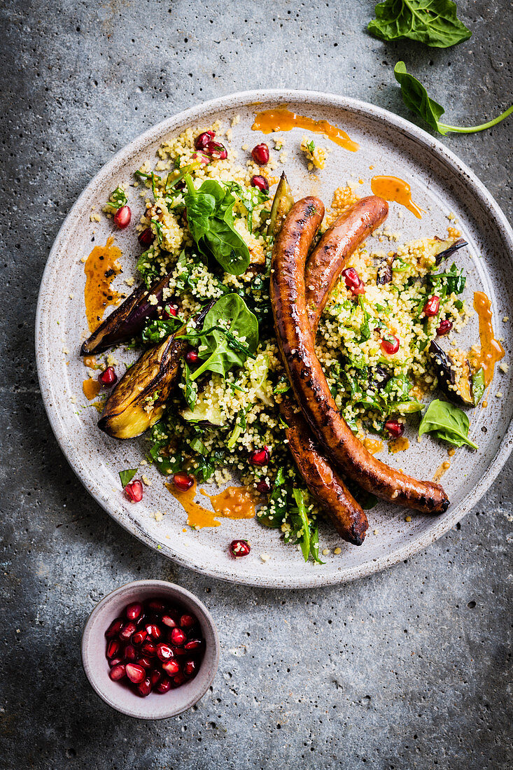 Merguez sausages served with couscous with aubergines, spinach and pomegranate seeds
