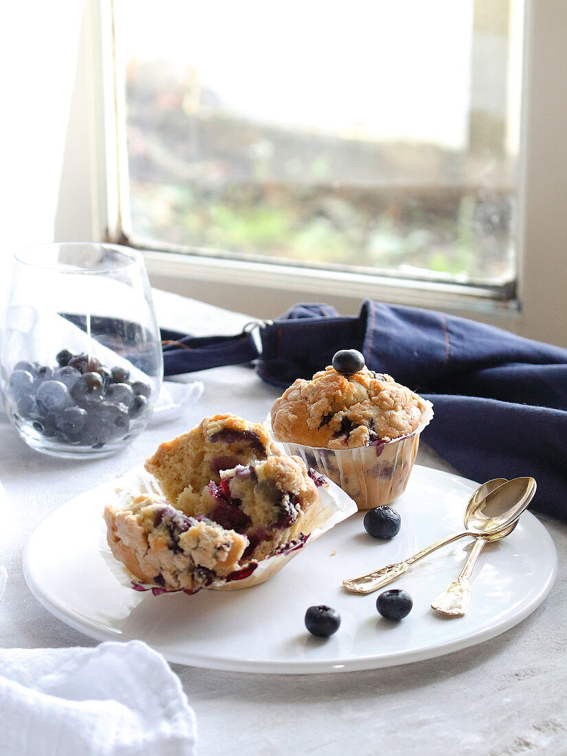 Blueberry muffins on a serving platter in front of a window