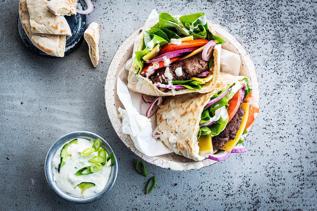 Pita burgers with tomatoes, onions and salad served with tzatziki