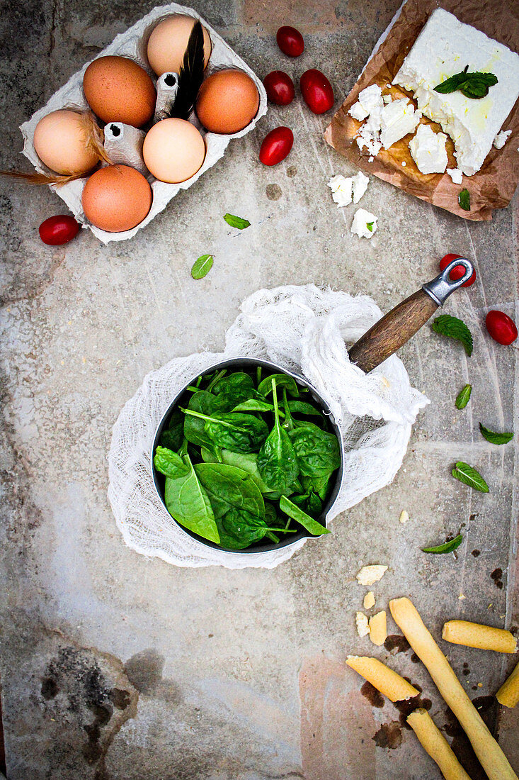 Still life with spinach, feta, eggs, grissini, and other ingredients