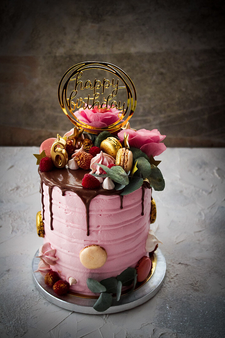 Pink birthday cake decorated with flowers and macarons