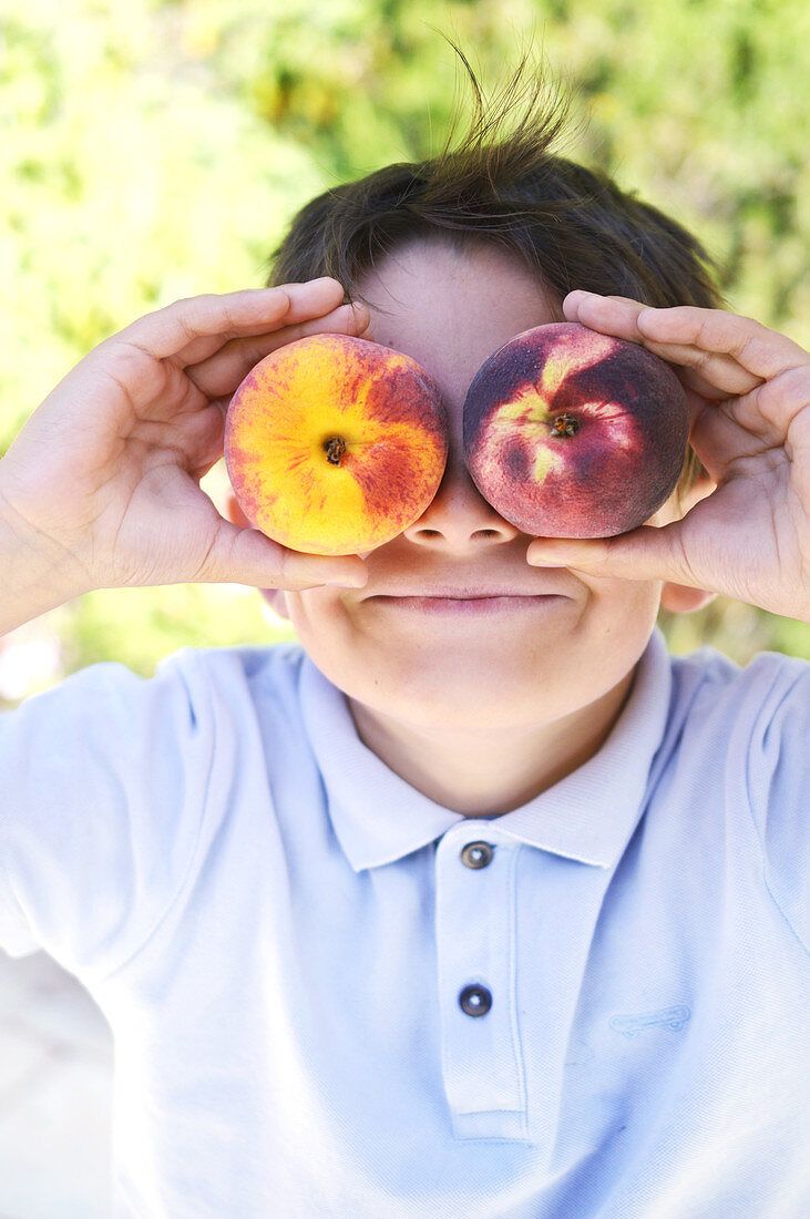 Kind hält sich zwei Pfirsiche vor die Augen