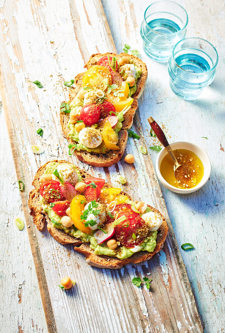 Slices of bread with avocado, cherry tomatoes, chickpeas and mozzarella cheese