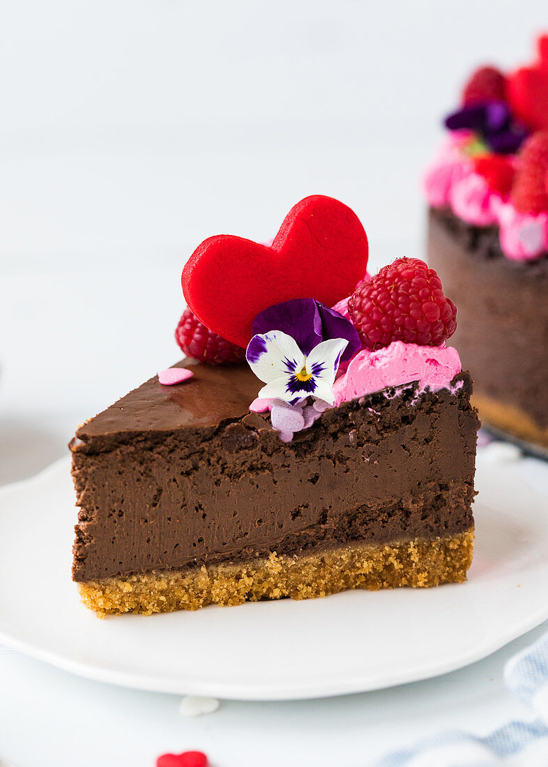 Ein Stück Schokoladen-Käsekuchen dekoriert mit Herz, Himbeeren und Blüte