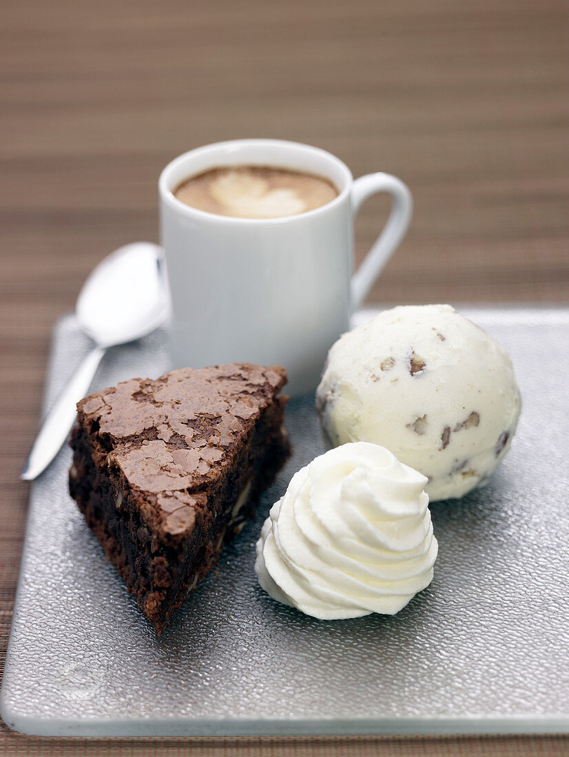 Ein Stück Schokoladenkuchen serviert mit Sahne, Eis und Kaffee