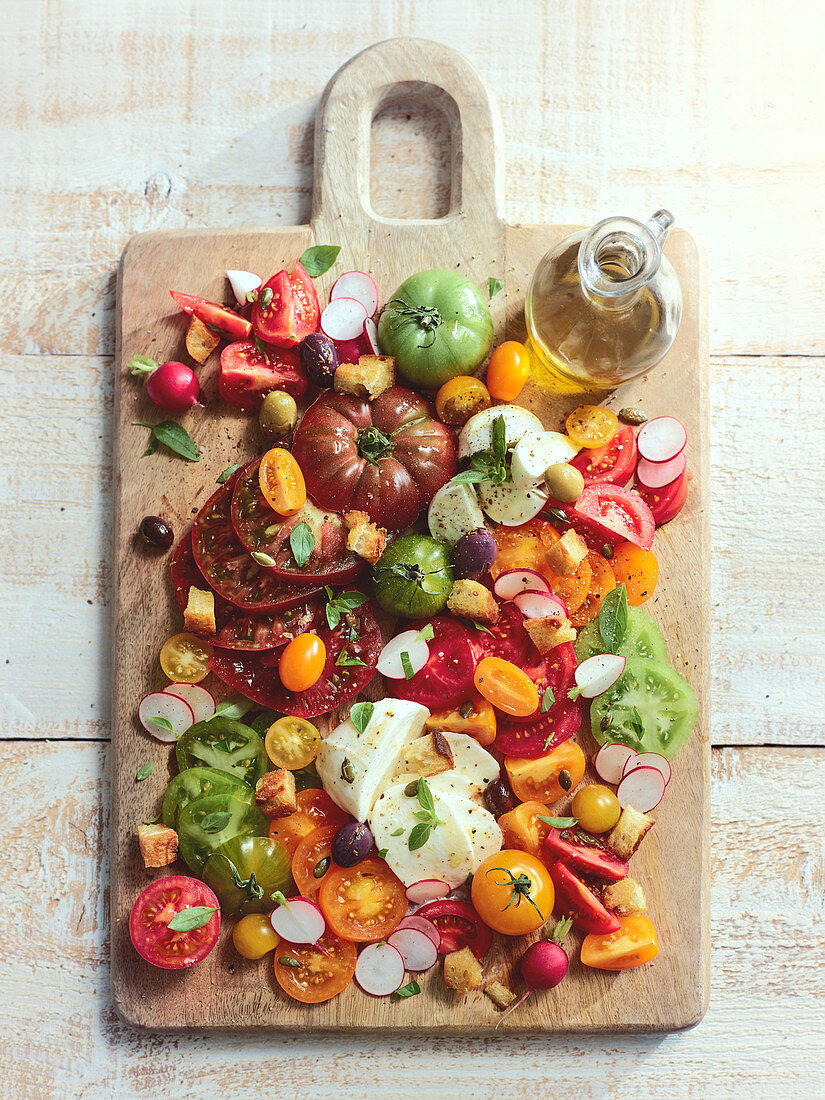 Heirloom-Tomaten mit Büffelmozzarella, Oliven und Olivenöl serviert auf Holzbrett