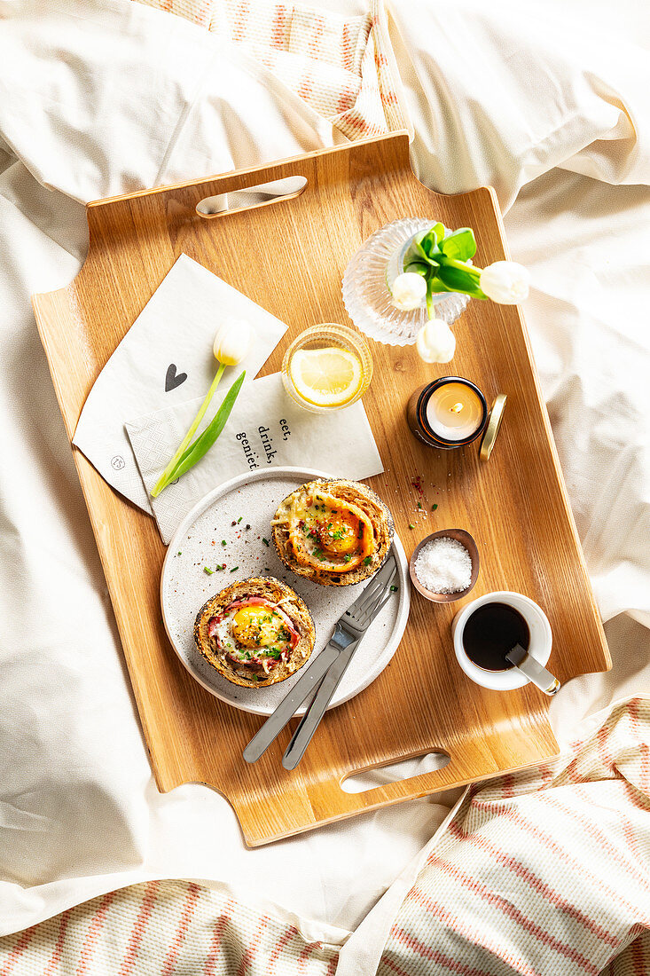 Gefülltes Brötchen mit Ei dazu Kaffee und Blumen auf Frühstückstablett