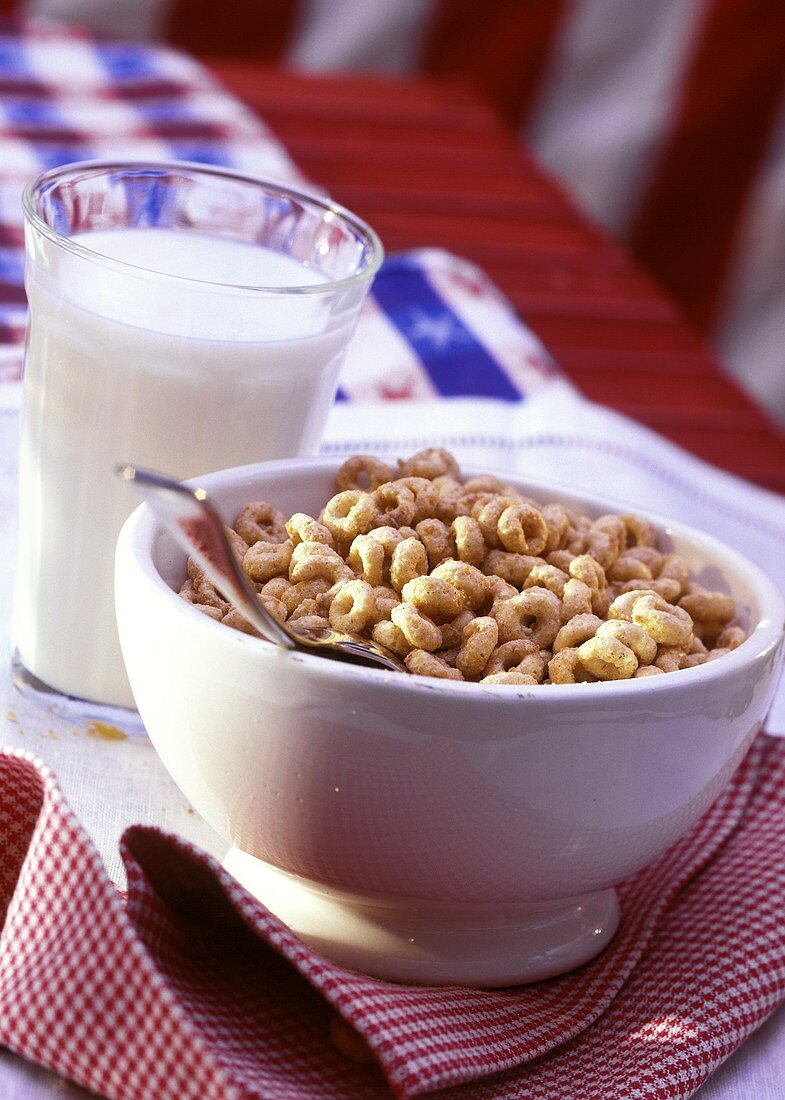 Ringförmige Cerealien (Cheerios) in weisser Schale; Milchglas