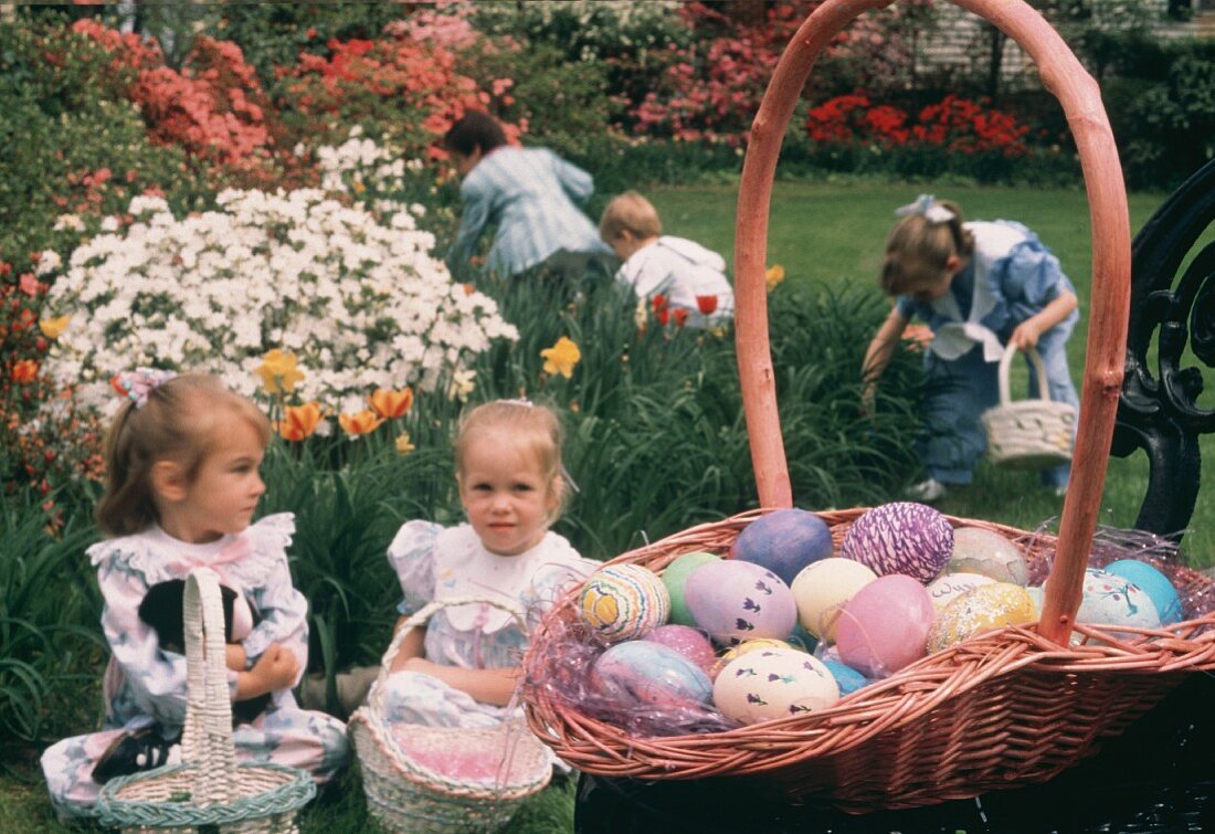 Sitzende Kinder mit Osterkörben & suchende Kinder im Garten