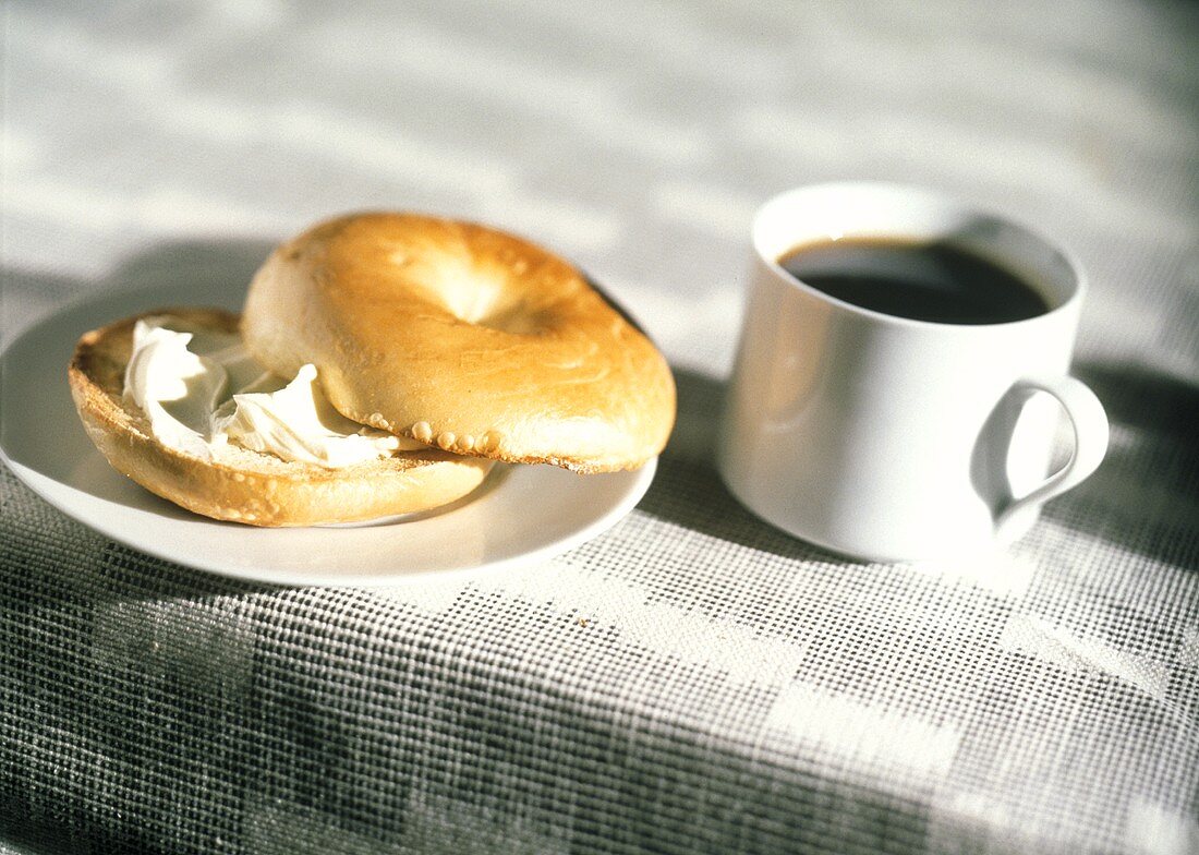 Bagel mit Frischkäsecreme auf kleinem Teller und Tasse Kaffee