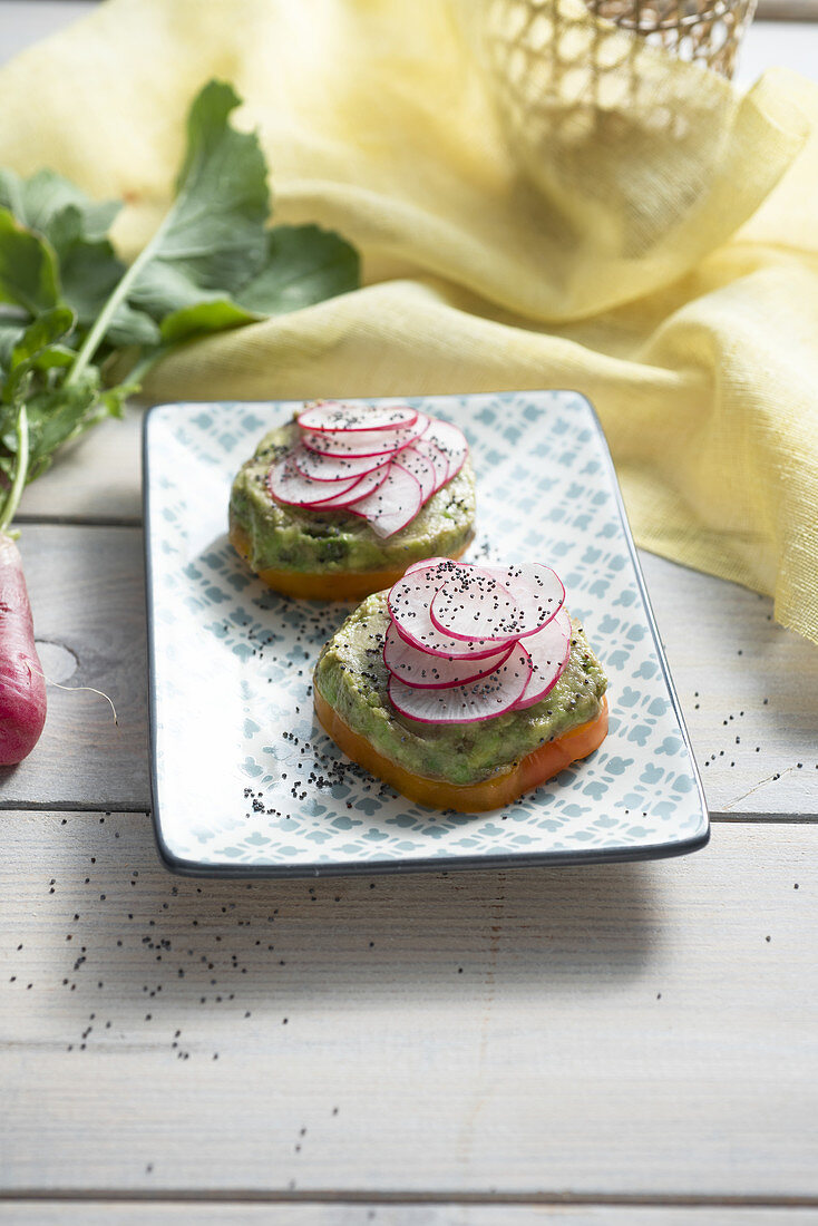 Yellow tomato slices topped with guacamole and sliced radishes