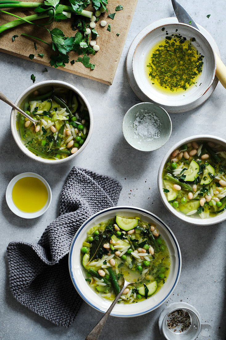 A vegetarian minestrone soup made with green beans, peas, zucchini, white beans and orzo pasta, served with a parsley, green onion, lemon and olive oil sauce