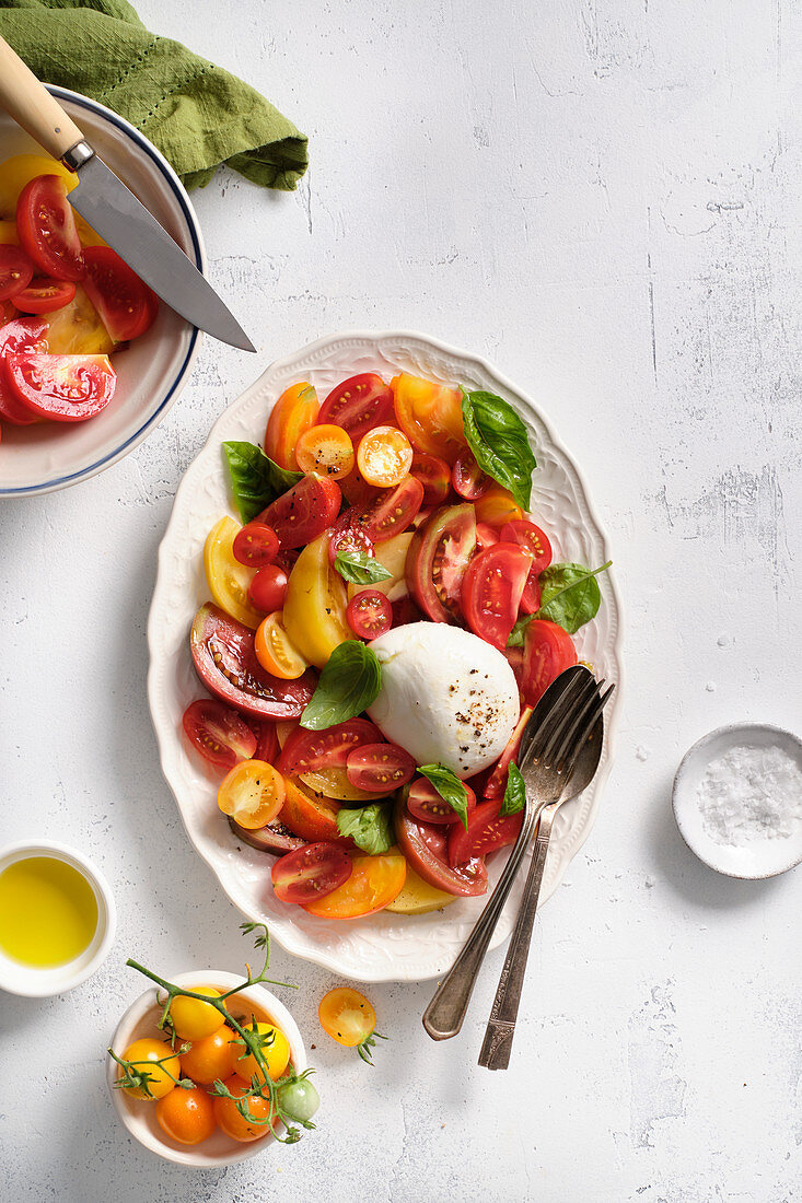 A salad of yellow, orange and red tomatoes with fresh basil and burrata cheese, seasoned with salt, black pepper and olive oil