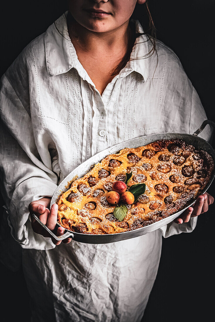 Person holding clafoutis with plums