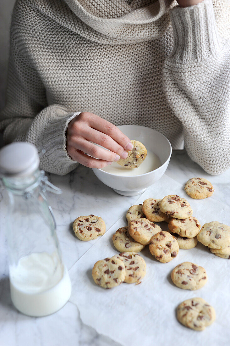 Frau tunkt Cocolate Chip Cookies in Schälchen mit Milch