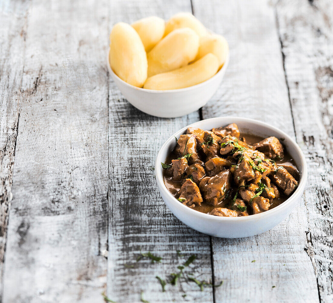 Bowl of pork with gravy served with boiled potatoes