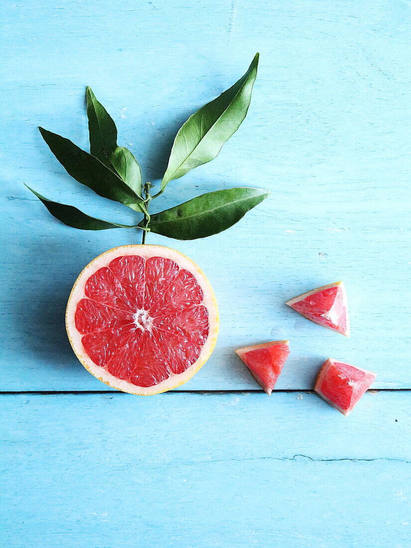 Grapefruit-Hälfte und Grapefruitstückchen auf blauem Untergrund