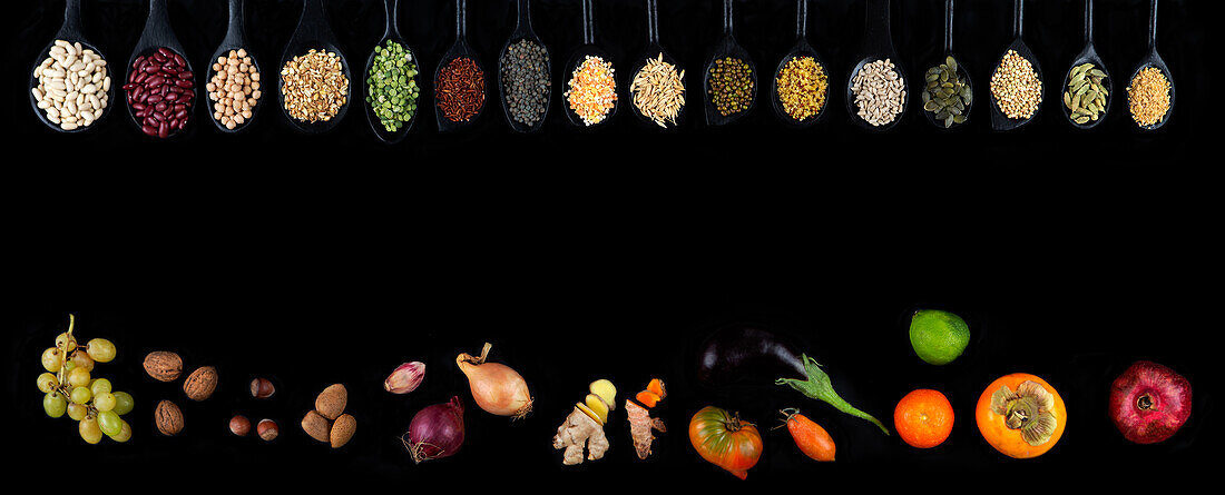 Legumes, seeds and cereals on spoons, in front of fruit, vegetables and nuts