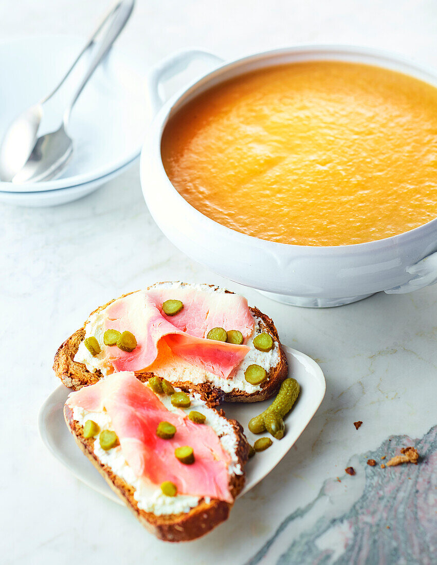 Cream of vegetable soup and bread with cream cheese, ham and gherkins