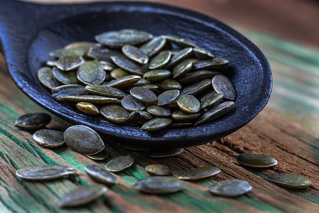 Pumpkin seeds on spoon against a wooden background (Close Up)