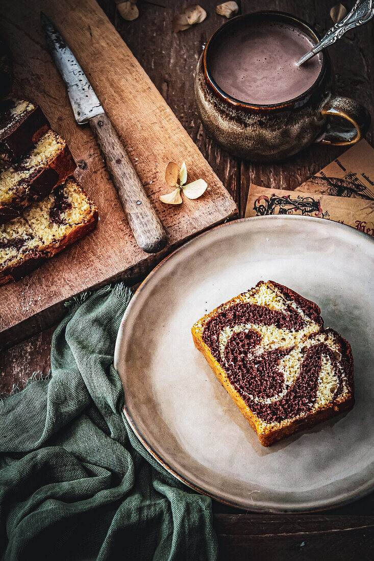 Ein Stück Marmorkuchen auf Teller dazu eine Tasse heiße Schokolade