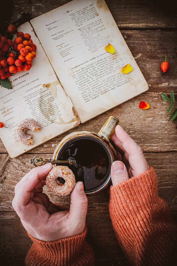 Woman's hands holding a cup of tea and small donut