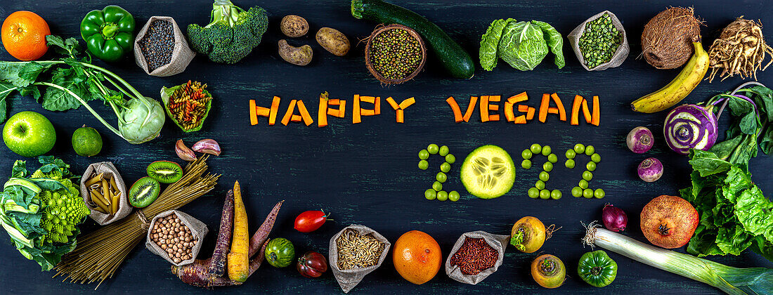 Schriftzug 'Happy Vegan 2022' umgeben von Obst, Gemüse und Getreide