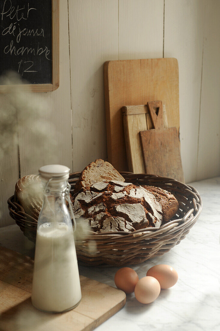 Stillleben mit Bauernbrot im Korb, Milch und Eier