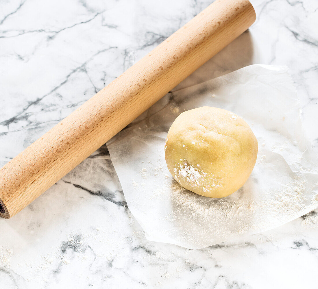 Shortcrust dough formed into a dough ball, dough roller next to it