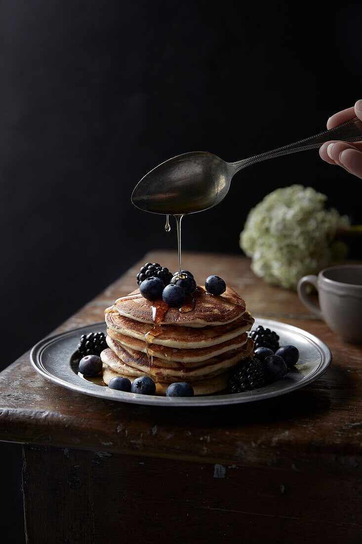 Stacked pancakes with blueberries, blackberries and honey