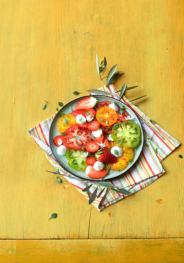 Salat aus bunten Tomaten mit Mini-Mozzarella und Erdbeeren auf gelbem Untergrund
