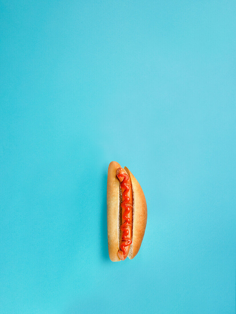 Hotdog mit Würstchen und Ketchup vor türkisfarbenem Hintergrund