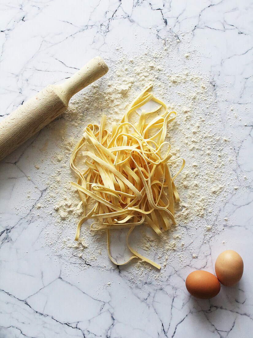 Fresh tagliatelle, eggs and a rolling pin on a marble work surface
