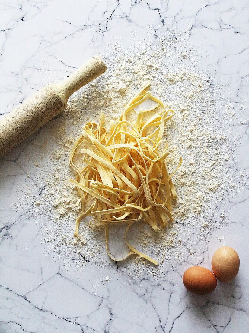 Frische Tagliatelle, Eier und Nudelholz auf Marmorarbeitsfläche