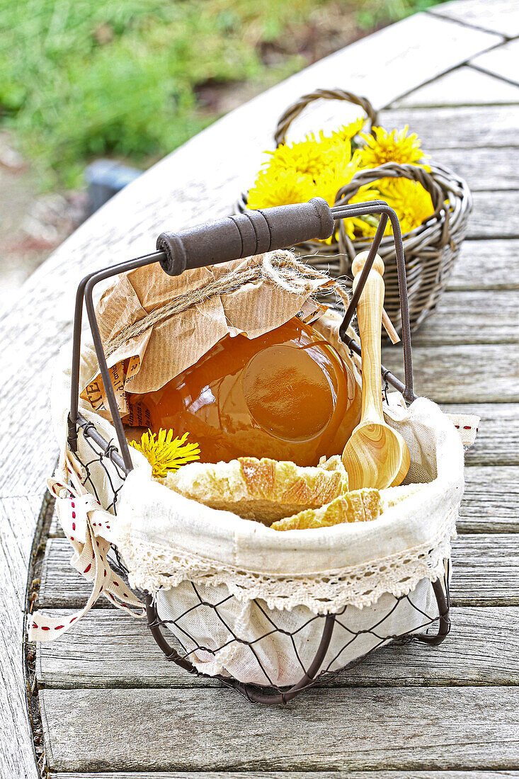 Jar of dandelion jelly with bread in wire basket on outdoor table