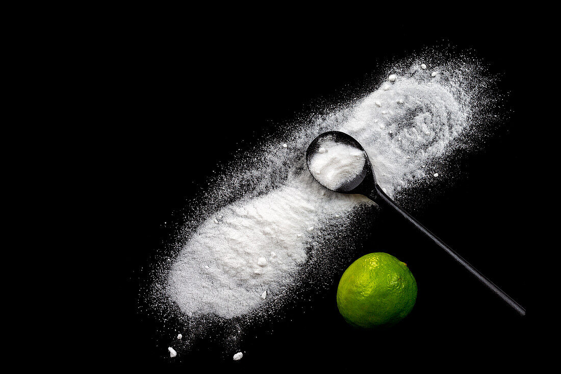 Baking powder on a black background next to a lime