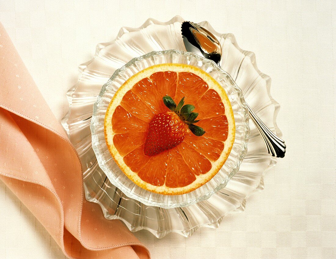 Halbe rosa Grapefruit mit Erdbeere in Glasschale mit Löffel