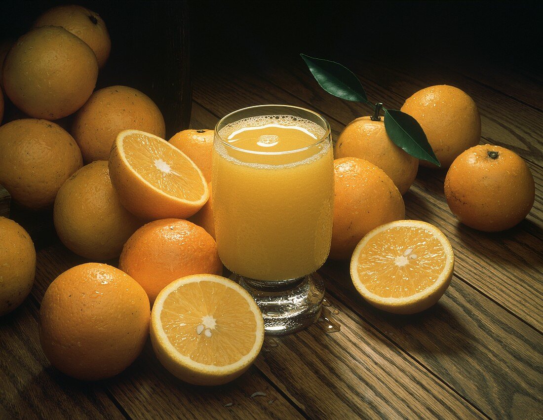 Ein Glas Orangensaft umgeben von ganzen & halbierten Orangen