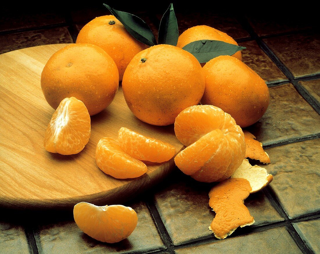Mehrere ganze Tangerinen & eine geschälte auf Holzteller