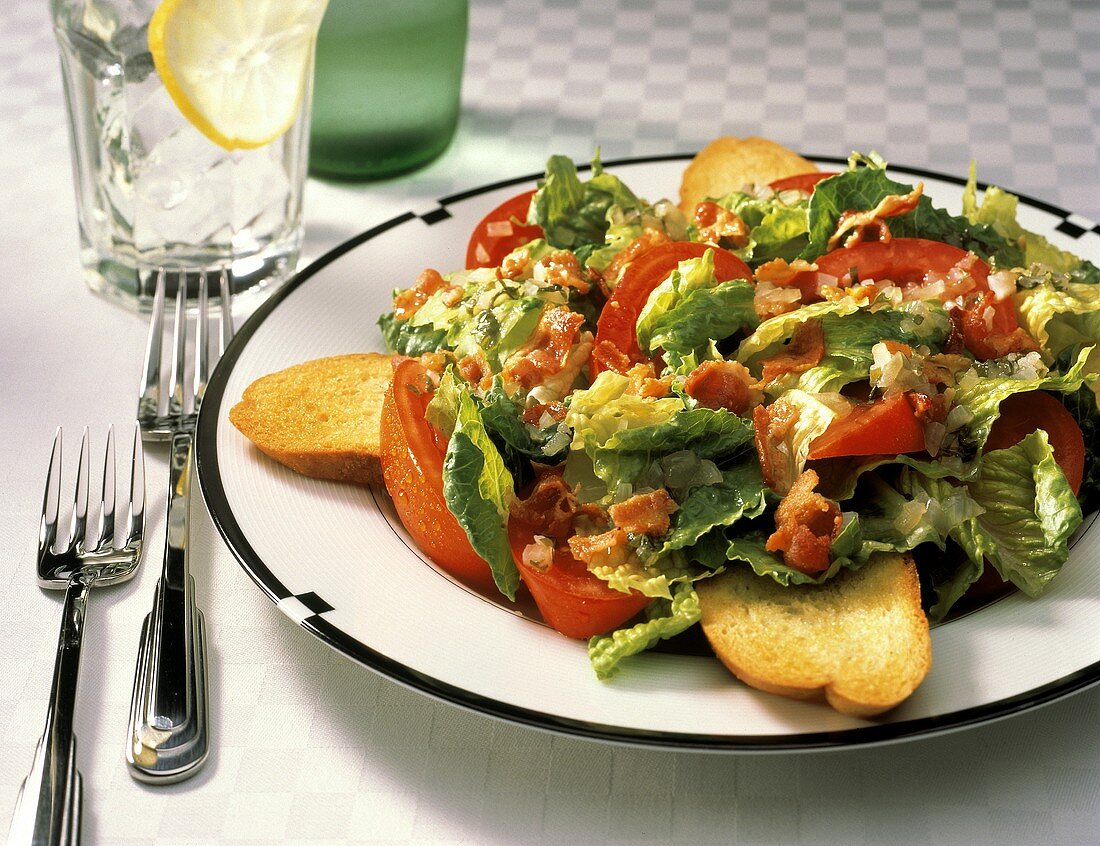 Blattsalat mit Speck, Tomaten & Weissbrotscheiben auf Teller