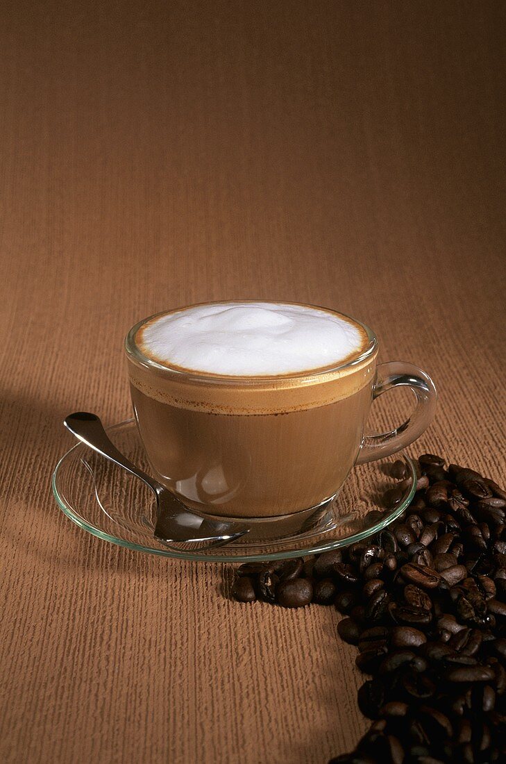 Cappuccino in Glastasse, daneben Kaffeebohnen