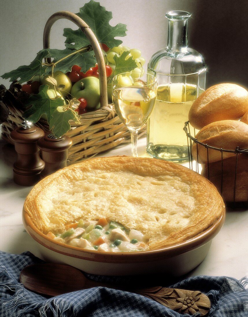 Chicken and vegetable pie in baking dish; wine, bread, fruit