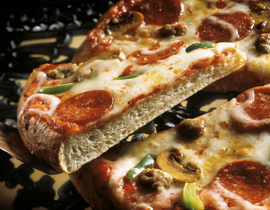 Pizza mit Paprikawurst, Käse u.a., ein Stück angehoben