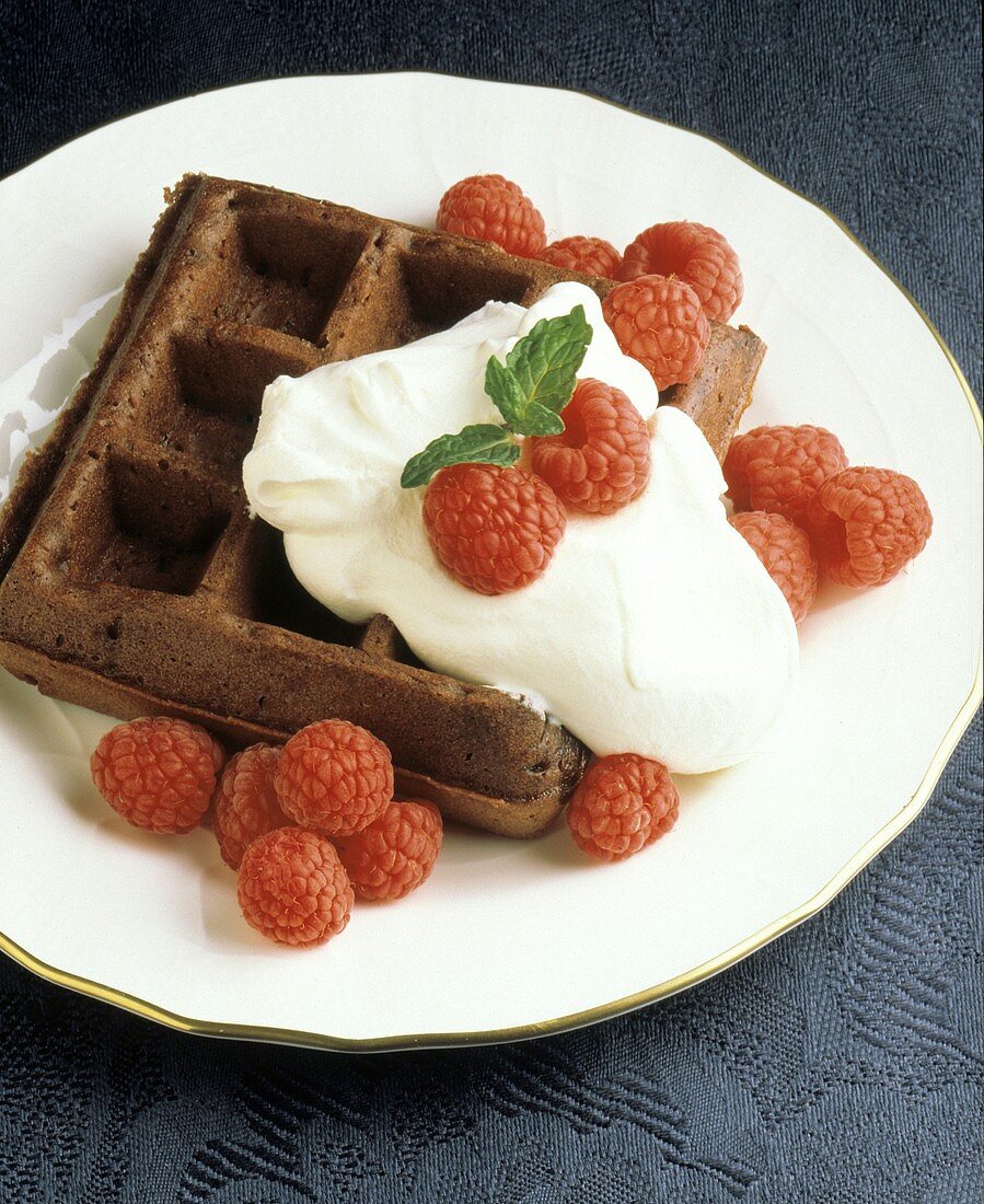 A chocolate waffle with raspberries and whipped cream