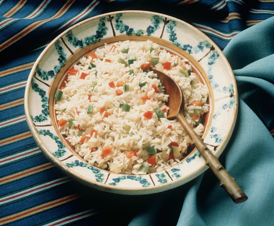 Würziger Reis mit Paprikawürfeln auf Teller mit Holzlöffel