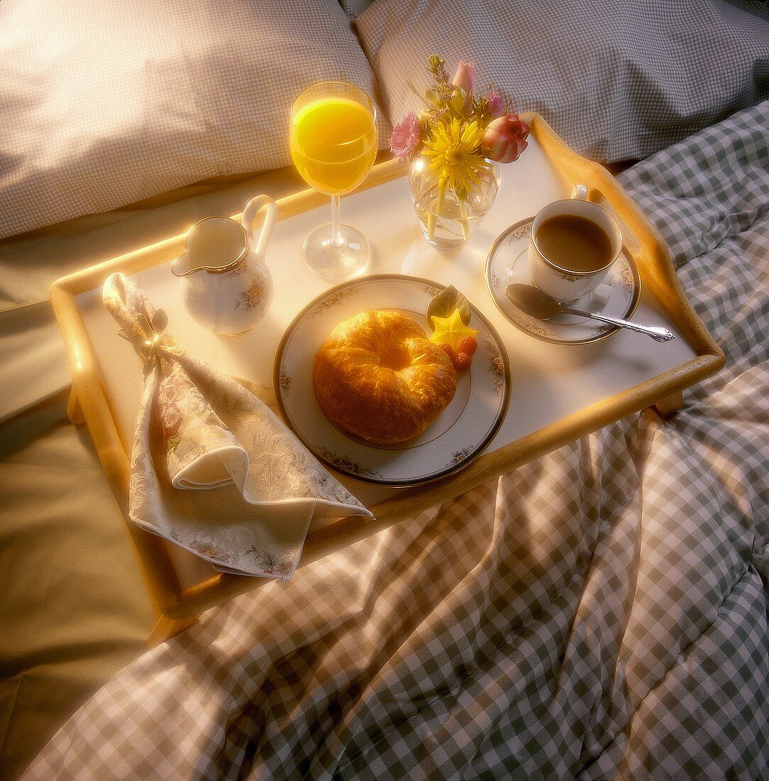 Frühstückstablett mit Croissant, Kaffee & Saft auf dem Bett