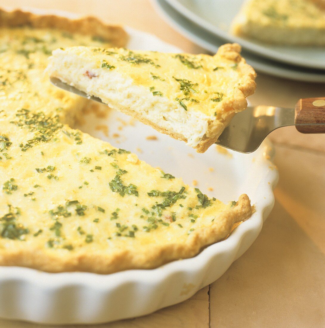 Quiche mit Schnittlauch in Auflaufform, ein Stück angehoben