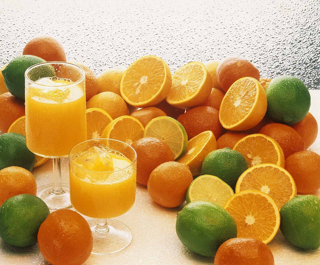 Zwei Gläser Orangensaft vor Orangen & Limetten