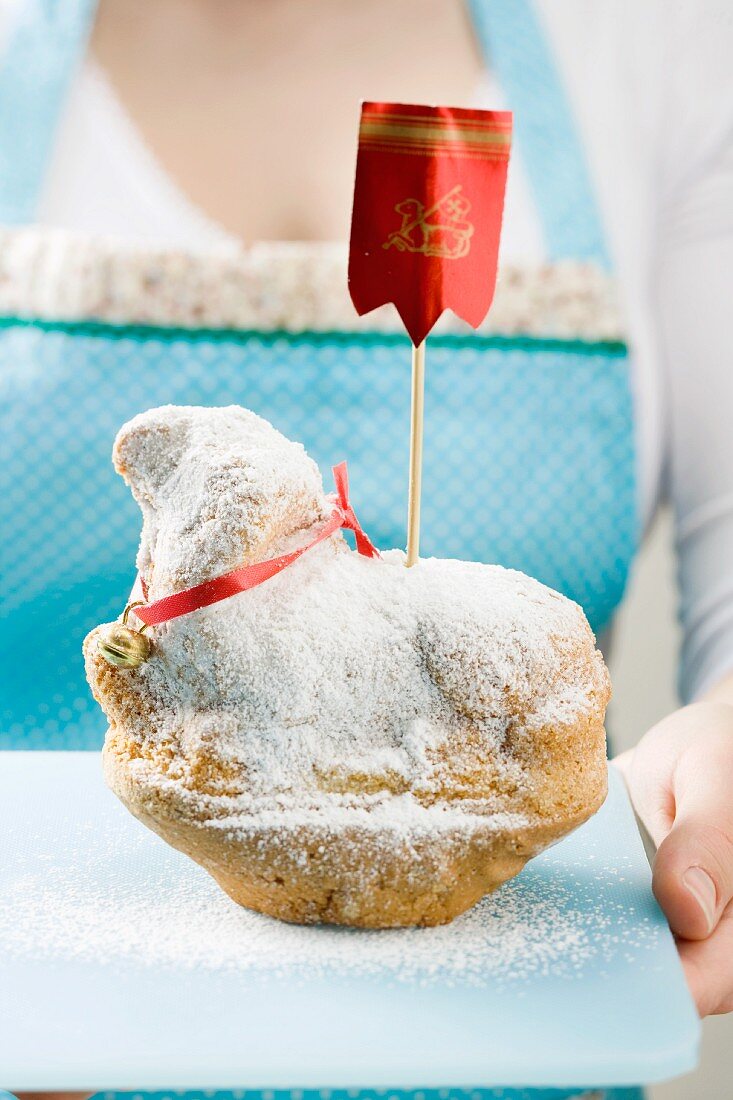 A woman serving a sweet Easter lamb dusted with icing sugar and decorated with a flag