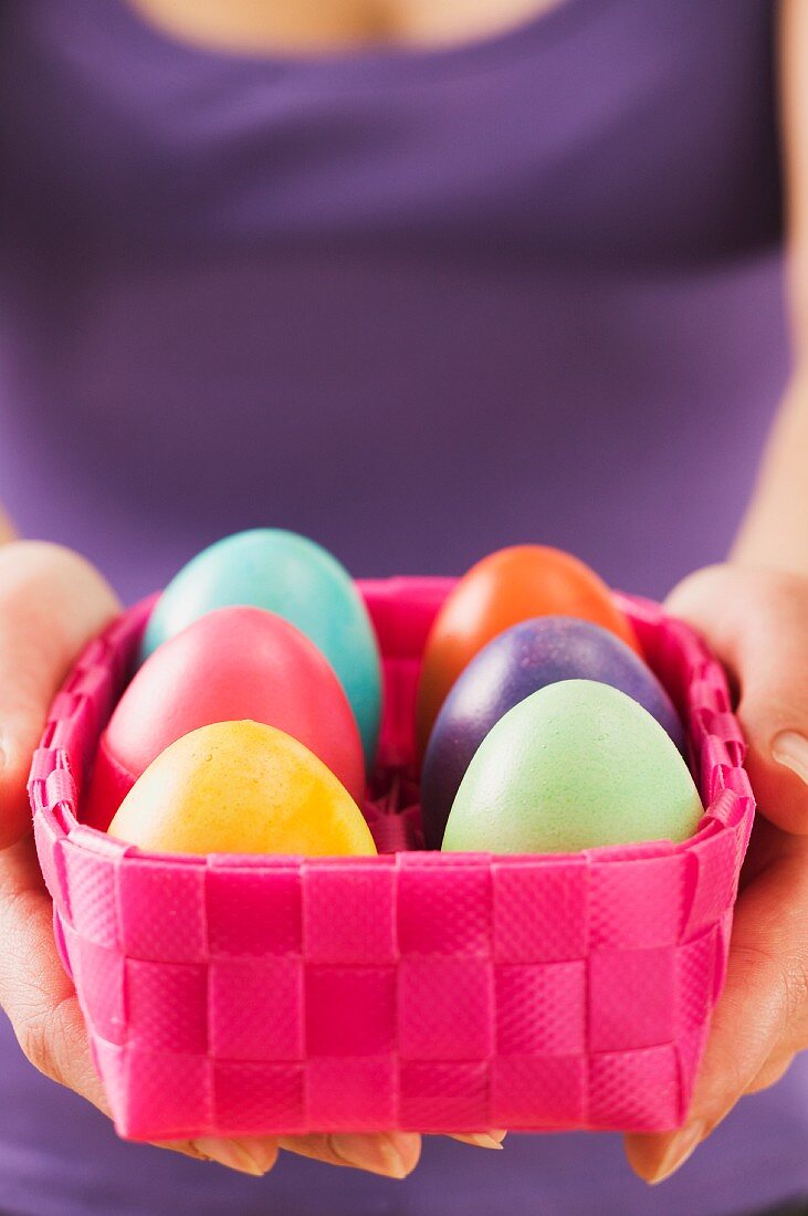 A woman holding a basket of coloured eggs